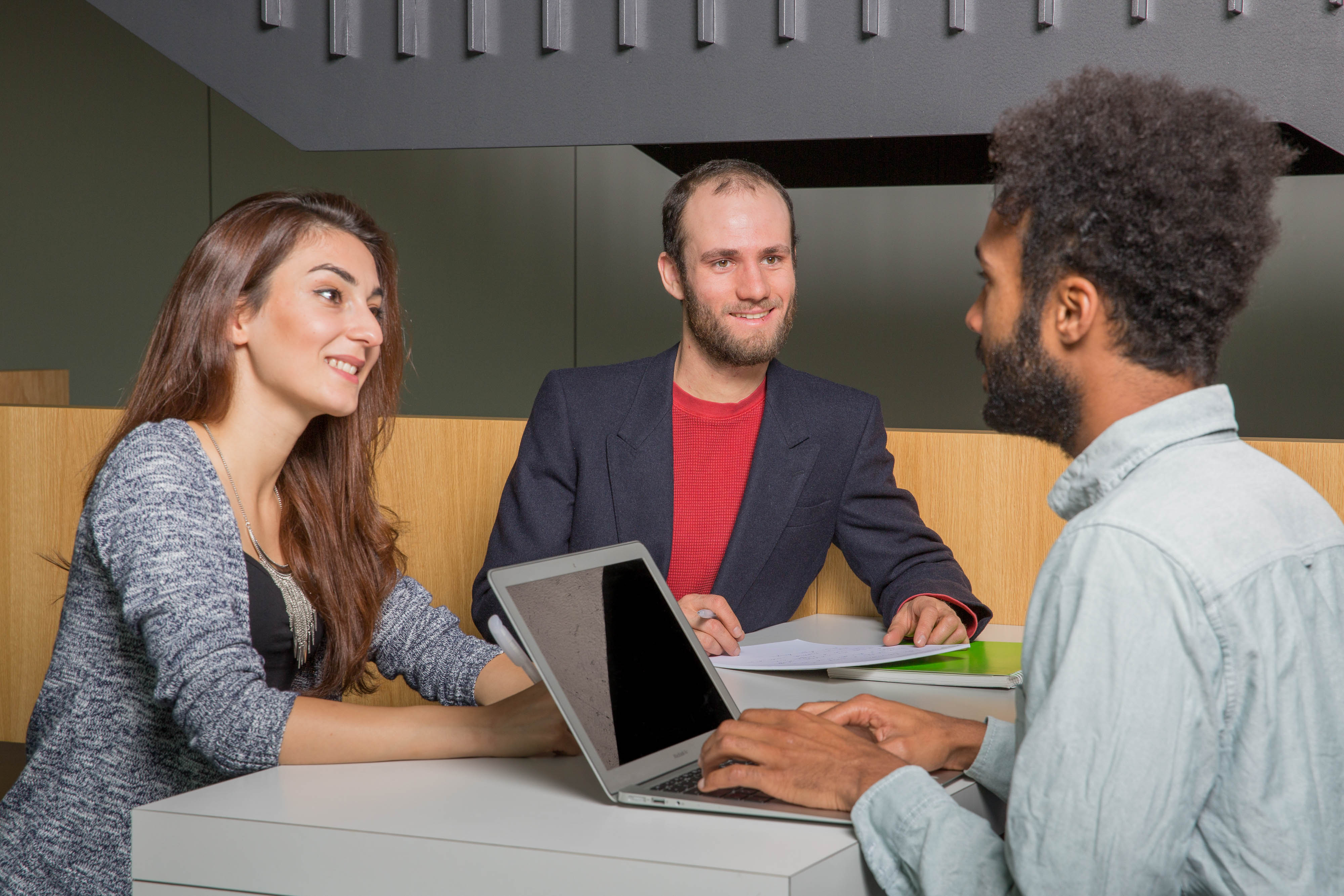 Three students sit opposite each other and they are talking.