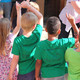 Kinderbetreuung Eine Gruppe von Kindern mit grünen T-Shirts sind von hinten zu sehen und melden sich.