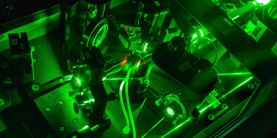 Eine Detailaufnahme eines Lasers im Labor in dunkel grünen Farben.