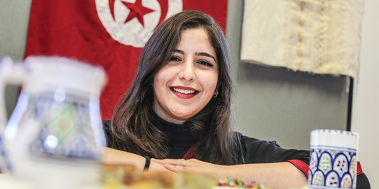 Internationale Studierende vor tunesischer Flagge Eine internationale Studierende lächelt in die Kamera. Im Hintergrund hängt eine Tunesienflagge.