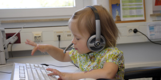 Kleinkind mit Kopfhörern tippt auf Tastatur.