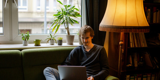 Ein Student, auf dem Sofa sitzend, arbeitet am Laptop.