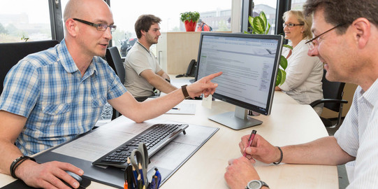 A man sits across from another man in a consulting situation from the ITMC service desk.