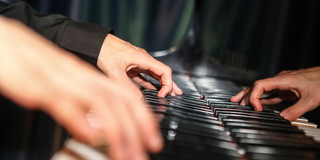 Zwei Hände spielen Klavier.