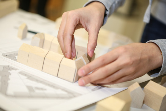Person puts wooden blocks Detail view of two hands placing wooden elements into a city model