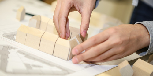 Zwei Hände stellen Bausteine auf, um ein Modell zusammenzusetzen.