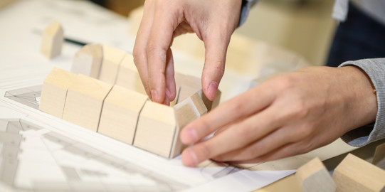 Two hands place building blocks to assemble a model.