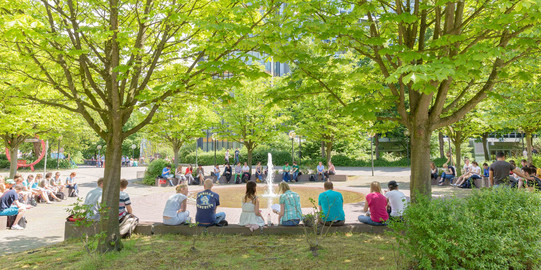 Studierende sitzend am Springbrunnen auf dem Campus Nord im Sommer