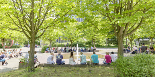 Studierende sitzend am Springbrunnen auf dem Campus Nord im Sommer