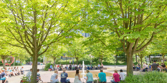 Studierende sitzend am Springbrunnen auf dem Campus Nord im Sommer