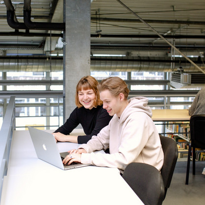 Zwei Studierende sitzen in der Bibliothek am Tisch und arbeiten an einem Laptop