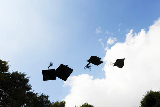 Four black graduation caps are thrown in the air.