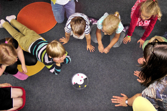 Eine Gruppe Kinder sitzen und liegen auf dem Boden im Kreis um eine Dose herum.