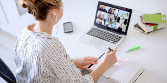 Digitales Lernen Am Schreibtisch sitzende Studentin schaut Lernvideos, daneben liegen Bücher und Stifte.
