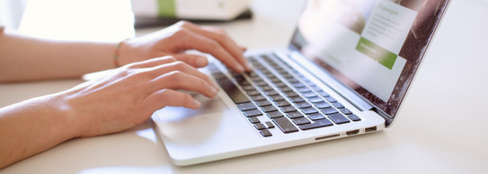 Studentin tippend am Laptop, daneben liegen Bücher.