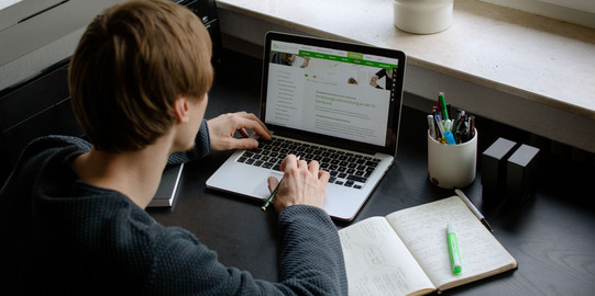 Ein Student arbeitet mit Laptop und Notizbuch.