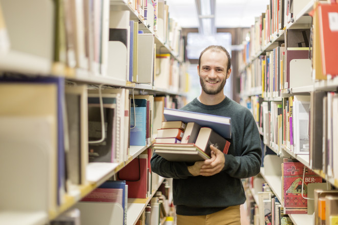 A student in a library holding books in his hands