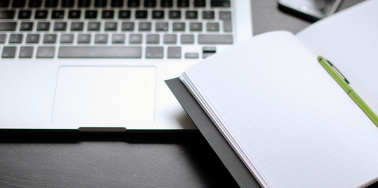 Laptop und Notizbuch Laptop und Notizbuch mit Stift auf einem Tisch liegend.