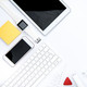 In weiß und gelb gehaltene Gegenstände für die Organisation: Tablet. Büroklammern, Schere, Smartphone, Notizblock, Uhr, Tastatur, Post-It, Thesafilm, Lineal. 