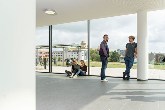 Studierende im Gespräch vor einem großen Fenster.