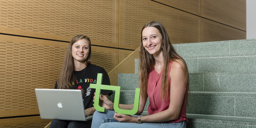 Zwei Studentinnen sitzen mit Laptop und TU-Logo auf einer Treppe.
