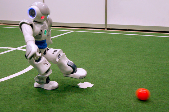 Soccer robot kicks A little white robot kicking a red ball on a soccer field.