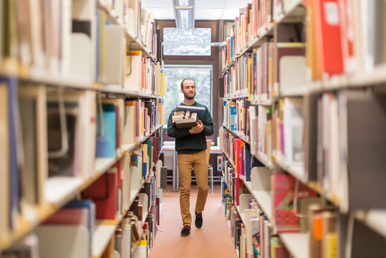 Student in the library Student walks along the bookshelves in the library.