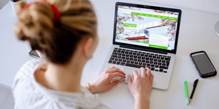 Am Schreibtisch sitzende Studentin tippt auf dem Laptop, daneben liegen Bücher und Stifte.
