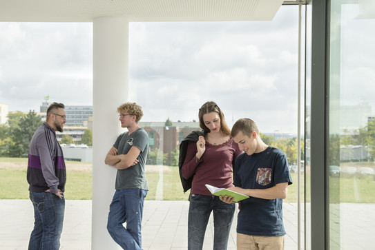 Studierende im Gespräch vor einem großen Fenster.