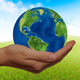 One hand holds a globe against the background of a green meadow with a blue sky.