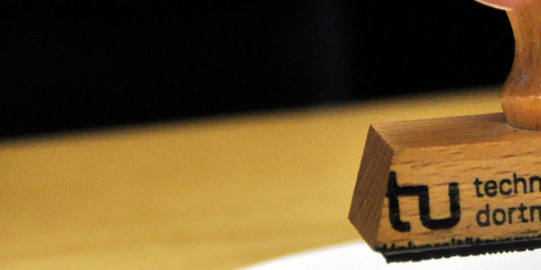 Stempel der TU Dortmund Nahufnahme eines TU Dortmund-Stempels über einem Blatt Papier
