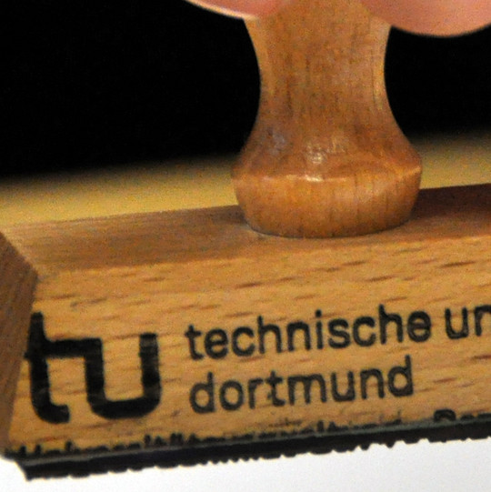 Nahufnahme eines TU Dortmund-Stempels über einem Blatt Papier