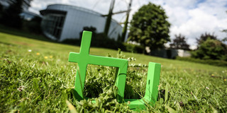 TU-Logo Im Vordergrund steht das TU-Logo im Gras, im Hintergrund das Audimax.