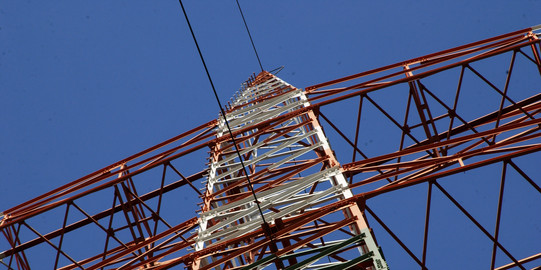 Ein Strommast von unten mit blauem Himmel im Hintergrund.