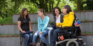 Studierende mit Behinderung Vier Studierende, darunter Studierende mit Behinderung, sitzen gemeinsam auf dem Campus.