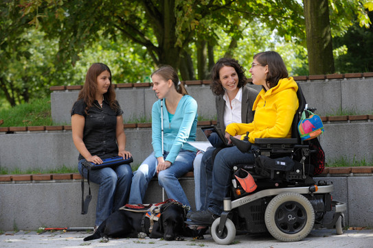 Students with disabilities Four women sitting outside on the campus, two of them with a white cane, one of them in a wheelchair