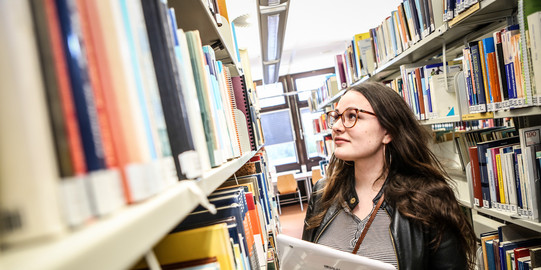 female student looking at a book shelf in the university library