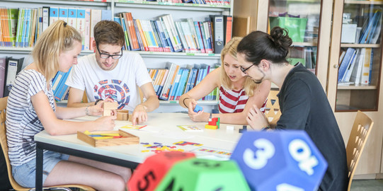 Vier Personen sitzen in der Mathedidaktik-Werkstatt am Tisch und bauen mit Würfeln.