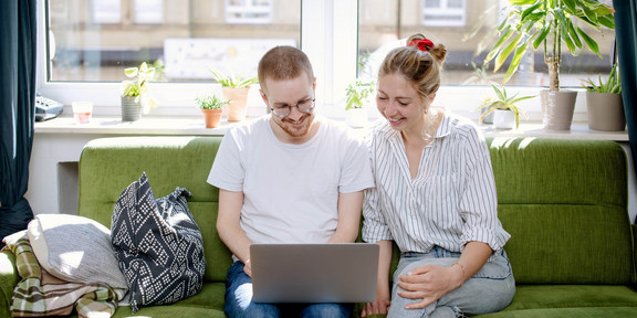 Zwei Studierende arbeiten am Laptop, auf einem Sofa sitzend.