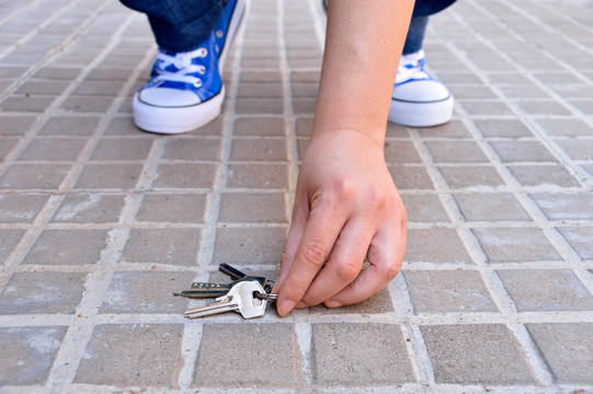 Close-up of hands picking up a bunch of keys from the street.