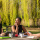 Studierende Drei Studierende sitzen an einem Sommertag an einer Sitzbank mit Tisch auf einer Wiese und unterhalten sich gut gelaunt.