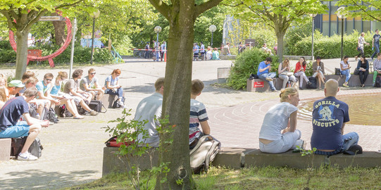 Studenten sitzen im Sommer am Brunnen des Martin-Schmeißer-Platzes