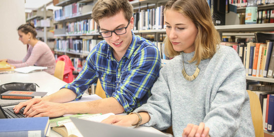Three students sitting at the table in the library and working.