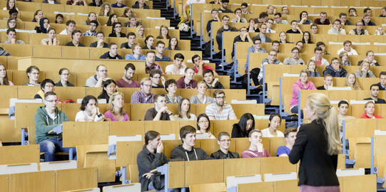 A lecturer stands in front of students in the lecture hall. 