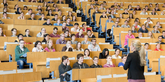 Eine Dozierende steht vor Studierenden in der Vorlesung im Hörsaal. 