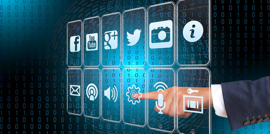 Auf einem dunkelblauen Hintergrund, der mit schwarzen 0en und 1en gespickt ist, sind mehrere App-Icons zu sehen, die auf weißumrandeten Displays dargestellt werden. Auf diese Displays zeigt der ausgestreckte Finger einer menschlichen Hand.