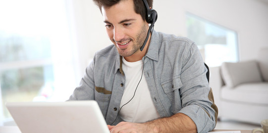 Mann in Videokonferenz Mann sitzt vor dem Laptop und hat ein Headset auf.