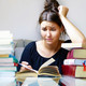 Eine Frau schaut angestrengt auf ein Buch, während sie ihren Kopf auf ihren Arm aufstützt.