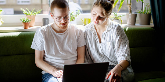 Two students working on a laptop, sitting on a sofa.