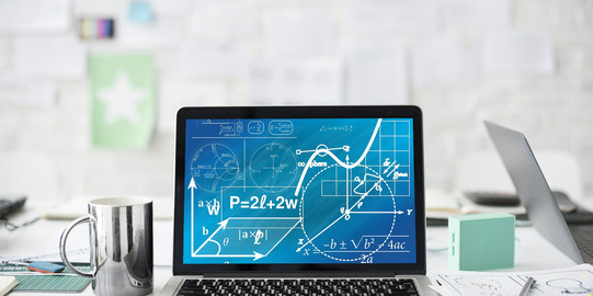 Laptop on a desk A laptop with mathematical formulas stands on a white desk next to a cup, pens and sheets of paper.